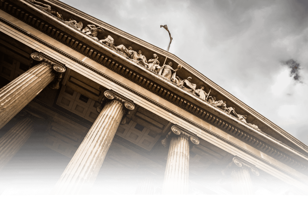 Low-angle view of a classical courthouse facade with tall columns and statues under a cloudy sky